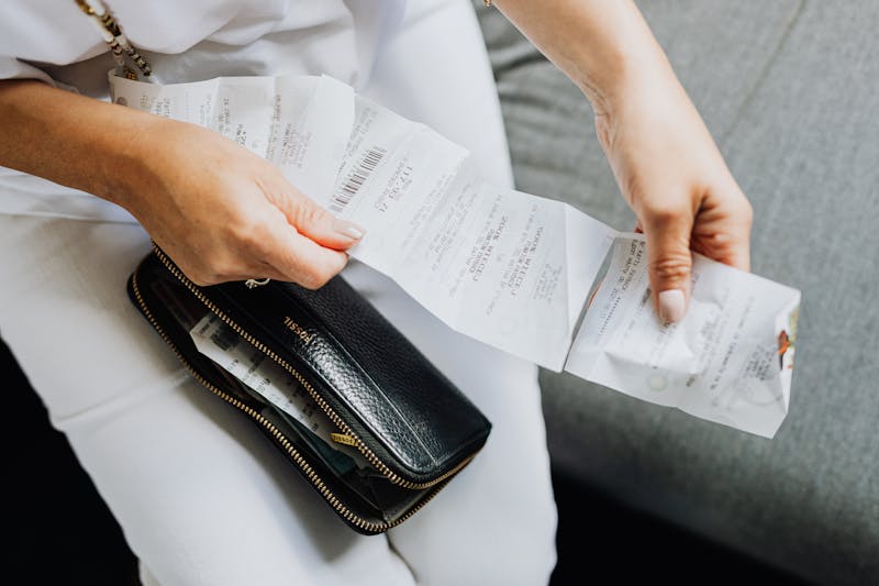 A person reviewing bank statements on a laptop with bills and a coffee mug, symbolizing hidden expenses draining money